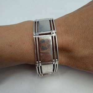 May include: A silver bracelet featuring a rectangular link design. The bracelet is made up of rectangular plates joined by vertical bars. The bracelet is worn on a wrist.