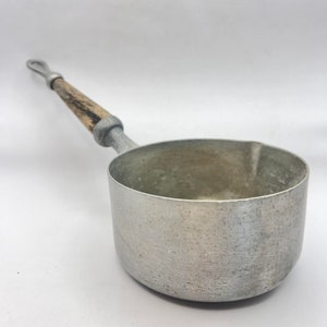 Könnte beinhalten: Ein silberner Aluminiumtopf mit einem Holzgriff. Der Topf hat einen leicht abgerundeten Boden und eine glatte, leicht strukturierte Oberfläche.