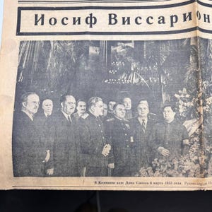 May include: A black and white photograph of a newspaper page featuring a group of men in suits and military uniforms. The headline reads in Cyrillic script. The image is a historical document.