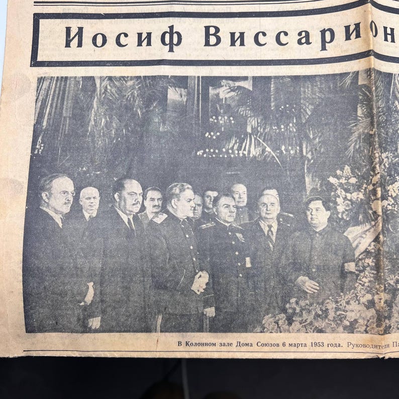 May include: A black and white photograph of a newspaper page featuring a group of men in suits and military uniforms. The headline reads in Cyrillic script. The image is a historical document.