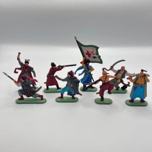 Peut inclure: Un ensemble de neuf figurines en plastique représentant des Cosaques, un groupe militaire historique. Les figurines sont peintes dans différentes couleurs, notamment le rouge, le bleu, le vert et le jaune. Certaines figurines tiennent des épées, tandis que d'autres tiennent des drapeaux ou des fusils. Les figurines sont debout sur un fond blanc.