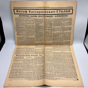 May include: An open vintage newspaper with text in a foreign language. The headline reads "Iosif Vissarionovich Stalin" and "Bezmernaia Skorb Progressivnogo Chelovechestva". The newspaper is yellowed with age and has multiple pages of text.
