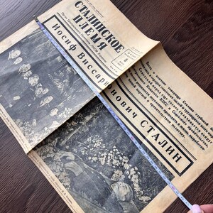 May include: An open vintage newspaper with the headline "STALINSKOE PLEMYA" and the name "IOSIF VISSARIONOVICH STALIN" in bold text. A measuring tape shows the newspaper is approximately 43 inches long. The newspaper has black and white images.