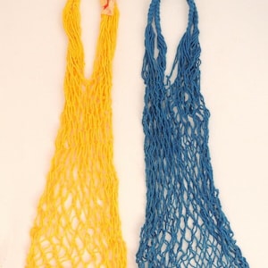 May include: Two string bags, one yellow and one blue. The bags are made of a knotted mesh material and are hanging from a white background.