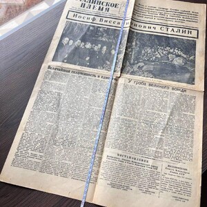 May include: An open vintage newspaper with text in Russian, featuring the headline "Stalin's Tribe" and the name "Iosif Vissarionovich Stalin." The newspaper is yellowed with age and has a measuring tape laid across it.