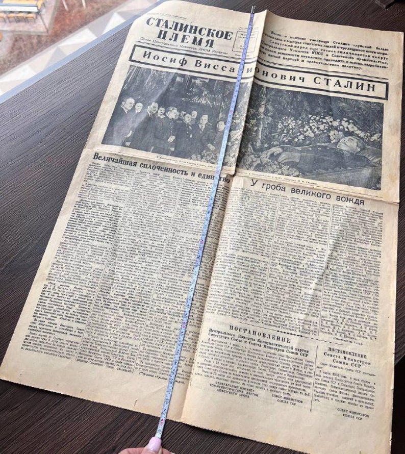 May include: An open vintage newspaper with text in Russian, featuring the headline "Stalin's Tribe" and the name "Iosif Vissarionovich Stalin." The newspaper is yellowed with age and has a measuring tape laid across it.