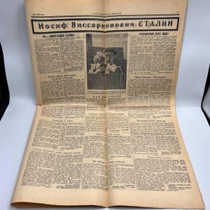 May include: A vintage newspaper with the headline "Iosif Vissarionovich Stalin" in bold Cyrillic letters. The newspaper is yellowed with age and features a portrait of a man in a military uniform. The text is in Russian.