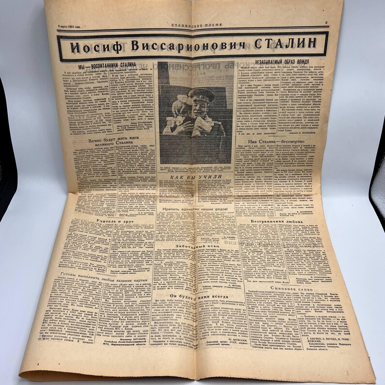 May include: A vintage newspaper with the headline "Iosif Vissarionovich Stalin" in bold Cyrillic letters. The newspaper is yellowed with age and features a portrait of a man in a military uniform. The text is in Russian.