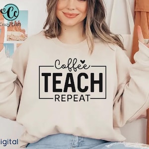 May include: A beige crewneck sweatshirt featuring black text that reads Coffee, TEACH, REPEAT inside a rectangular frame. The word Coffee is written in a cursive script with a small heart above it, while TEACH and REPEAT are in bold block letters.