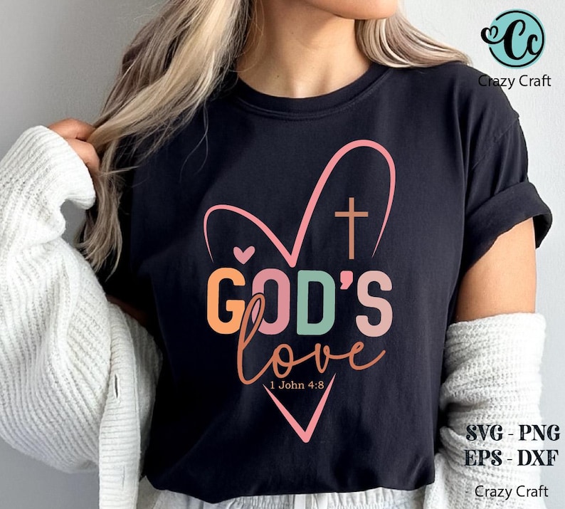 K&ouml;nnte beinhalten: Schwarzes T-Shirt mit einem herzf&ouml;rmigen Design und den Worten "GOD'S love" in bunten Buchstaben. Ein Kreuz befindet sich im Herzen, und der Bibelvers 1. Johannes 4,8 steht darunter. Das Crazy Craft-Logo befindet sich oben rechts.