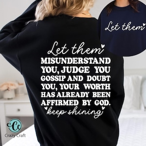 May include: Black sweatshirt with white text that reads "Let them misunderstand you, judge you, gossip and doubt you, your worth has already been affirmed by God. Keep shining." A navy blue sweatshirt with the words "Let them" is also shown.