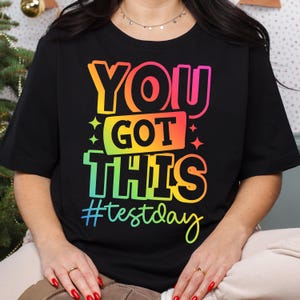 May include: Black t-shirt with the text "YOU GOT THIS" in a rainbow gradient, with the hashtag "#testday" in teal. The design includes star accents. The shirt is short-sleeved.