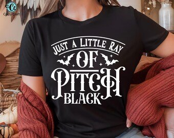 Puede incluir: Camiseta negra con el texto blanco "JUST A LITTLE RAY OF PITCH BLACK", adornada con murciélagos y estrellas. Una prenda informal.