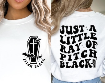 Puede incluir: Sudadera blanca con un gráfico negro de un ataúd, murciélagos y una araña, con las palabras "PITCH BLACK". La parte trasera de la sudadera tiene el texto "JUST A LITTLE RAY OF PITCH BLACK" en negro.