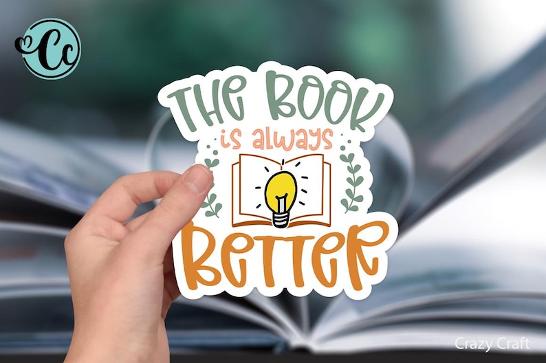 May include: A white sticker with the text "The book is always better" in orange and pink lettering. A lightbulb is inside an open book, with green leaves on either side.