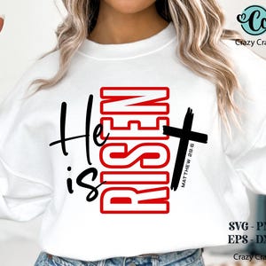 May include: White sweatshirt with the words "He is Risen" in black and red. A black cross is on the right side of the design, with "Matthew 28:6" printed vertically. The design is for Easter.