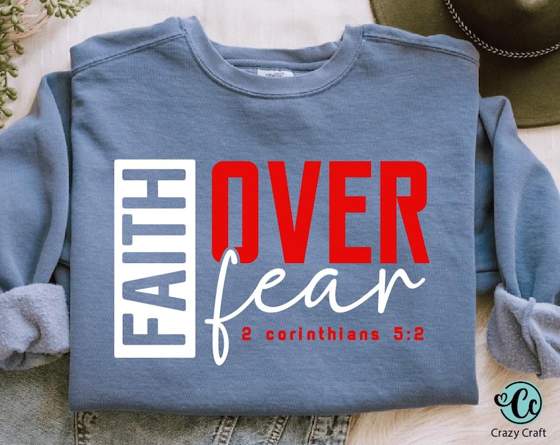 May include: A blue sweatshirt with the words "FAITH OVER fear" in red and white lettering. The text "2 Corinthians 5:2" is printed in white below the main text.