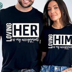Puede incluir: Dos camisetas negras con texto blanco. Una camiseta dice "LOVING HER is my assignment" y la otra "LOVING HIM is my assignment". Las camisetas son un conjunto a juego.