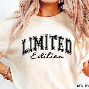 May include: Cream-colored t-shirt with the words "LIMITED Edition" in black, outlined in white, in a collegiate font. The text is centered on the shirt. The shirt has rolled-up sleeves.