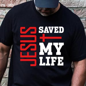 May include: A black t-shirt with the words "JESUS SAVED MY LIFE" in white and red lettering. A red cross is between the words "SAVED" and "MY".