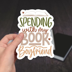 May include: A white sticker with brown and green lettering that reads "Spending with my Book Boyfriend". The sticker features a small open book with a heart above it.