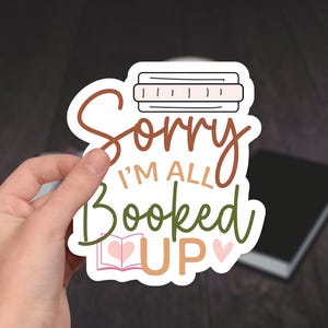 May include: A white sticker with brown and green lettering that reads "Sorry I'm all booked up" with a small book and hearts.