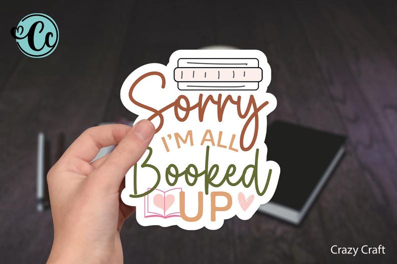 May include: A white sticker with brown and green lettering that reads "Sorry I'm all booked up" with a small book and hearts.