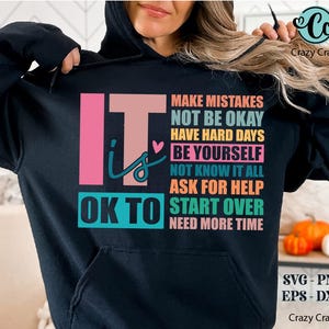 May include: Black hoodie with a colorful graphic that says "It is OK to" and lists a series of phrases including "Make Mistakes", "Not Be Okay", "Have Hard Days", "Be Yourself", "Not Know It All", "Ask For Help", "Start Over", and "Need More Time".