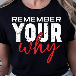 May include: Black t-shirt with the words "REMEMBER YOUR why" in white and red lettering. The text has a distressed, textured appearance. The shirt is a crew neck style.
