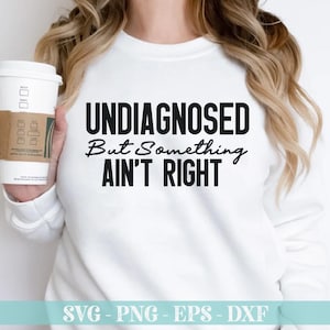 May include: White long-sleeve shirt with black text that reads "UNDIAGNOSED But Something AIN'T RIGHT".