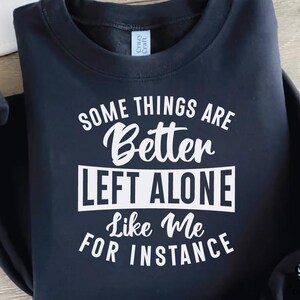May include: Navy blue sweatshirt with the text "SOME THINGS ARE Better LEFT ALONE Like Me FOR INSTANCE" in white. The sweatshirt has a crew neck and long sleeves. The brand tag "Crazy Craft" is visible.
