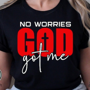 May include: Black t-shirt with the words "NO WORRIES GOD got me" in white and red. The word "GOD" is in a bold red font with a cross in the center. The shirt has a rolled sleeve.