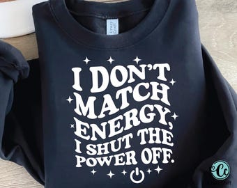 May include: A navy blue sweatshirt with the text "I DON'T MATCH ENERGY, I SHUT THE POWER OFF" in white, stylized lettering. The design includes star accents and a power button symbol. The sweatshirt has a crew neck and long sleeves.