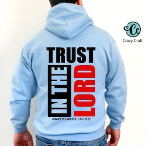 以下が含まれることがあります： 黒と赤で「TRUST IN THE LORD」の文字がプリントされた、水色のパーカー。「PROVERBS 16:20」の文字も。パーカーにはドローストリングフードとカンガルーポケットが付いています。Crazy Craftのロゴが右上に入っています。