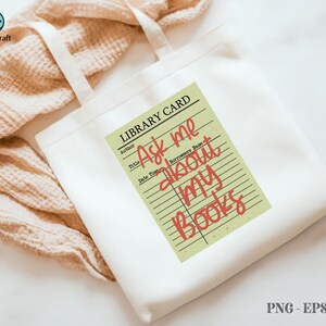 May include: White tote bag with cream-colored handles featuring a library card design. The card reads "Ask me about my books" in red script. The bag is on a beige textured surface.