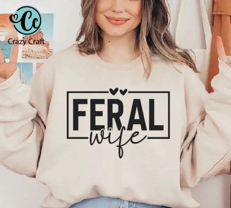 May include: A white sweatshirt with the text "FERAL wife" in black lettering inside a black rectangle. Two small hearts are above the rectangle.