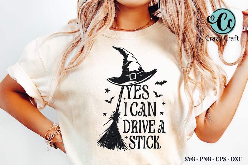 K&ouml;nnte beinhalten: Cremefarbenes T-Shirt mit schwarzem Hexenhut, Besen, Flederm&auml;usen und Sternen-Grafik. Der Text lautet "YES I CAN DRIVE A STICK." Das Crazy Craft-Logo befindet sich oben rechts.