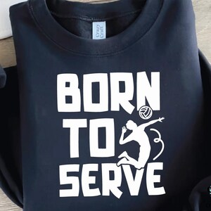 K&ouml;nnte beinhalten: Marineblaues Sweatshirt mit dem wei&szlig;en Schriftzug "BORN TO SERVE". Darunter befindet sich eine wei&szlig;e Silhouette eines Volleyballspielers beim Aufschlag. Das Sweatshirt hat einen Rundhalsausschnitt.