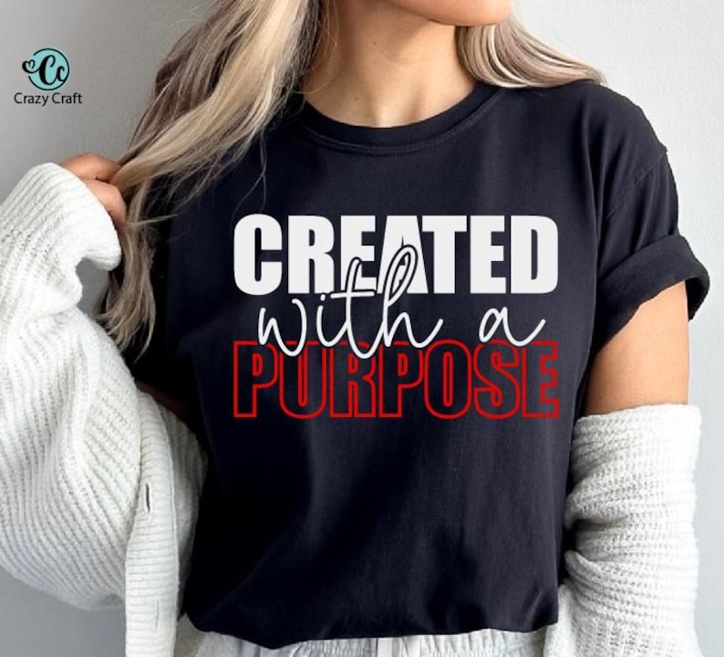 以下が含まれることがあります： 白と赤の文字で「CREATED with a PURPOSE」と書かれた黒いTシャツ。 シャツはクルーネックと半袖です。 Crazy Craftのロゴが左上にあります。