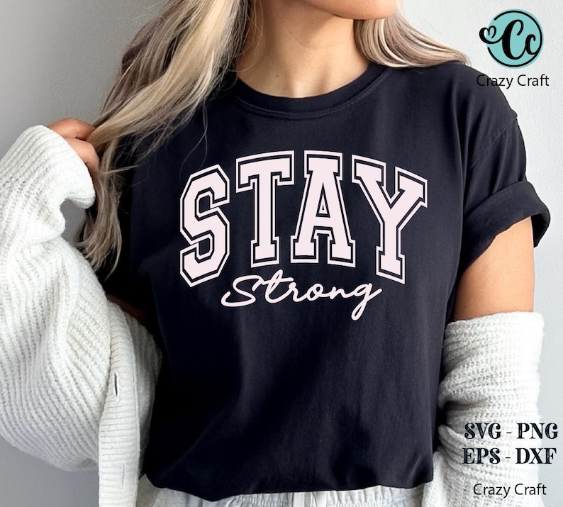 May include: Black t-shirt with the words "STAY Strong" in a pink, collegiate-style font. The shirt also has the text "Strong" in a cursive font. The shirt is a casual style.