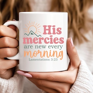 K&ouml;nnte beinhalten: Wei&szlig;e Keramiktasse mit dem Text "His mercies are new every morning" in Rosa, Orange und Gr&uuml;n. Das Design beinhaltet eine Sonne und eine Berg-Grafik. Die Tasse hat auch den Bibelvers Klagelieder 3:23.