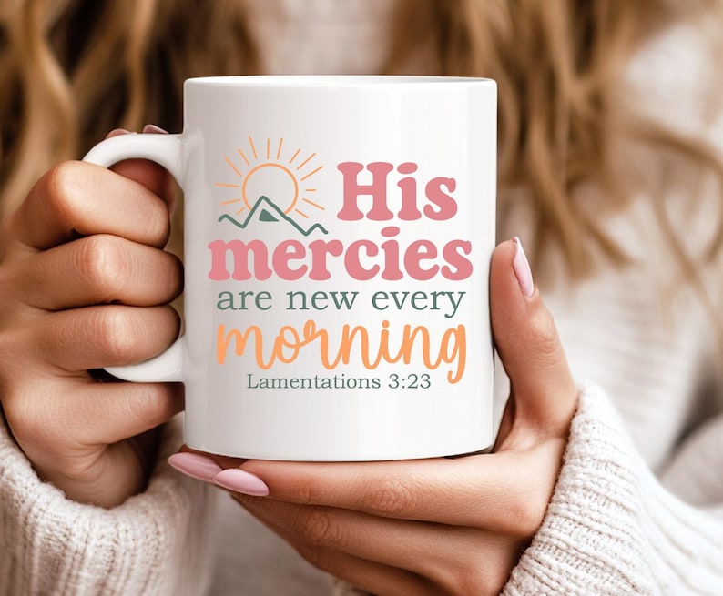 K&ouml;nnte beinhalten: Wei&szlig;e Keramiktasse mit dem Text "His mercies are new every morning" in Rosa, Orange und Gr&uuml;n. Das Design beinhaltet eine Sonne und eine Berg-Grafik. Die Tasse hat auch den Bibelvers Klagelieder 3:23.
