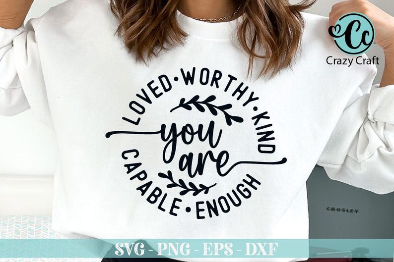 Pu&ograve; includere: Felpa bianca con un design circolare nero che dice "Loved-Worthy-Kind You Are Capable-Enough" con un piccolo disegno floreale su entrambi i lati del testo "You Are".
