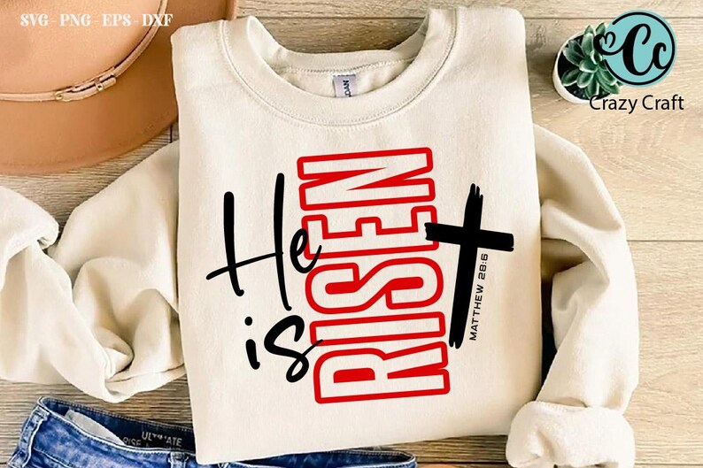 May include: Cream-colored sweatshirt with the text "He is Risen" in black and red, featuring a cross and the Bible verse Matthew 28:6. The design is centered on the front of the long-sleeved top.