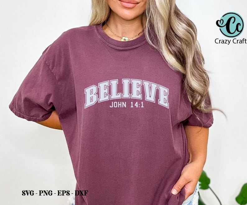 K&ouml;nnte beinhalten: Ein maroonfarbenes T-Shirt mit dem Wort "BELIEVE" in wei&szlig;en Buchstaben mit grauem Umriss. Der Text "JOHN 14:1" ist unter dem Wort "BELIEVE" gedruckt.