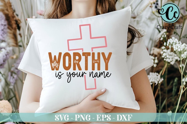 K&ouml;nnte beinhalten: Wei&szlig;es Kissen mit dem Text "WORTHY is your name" in Braun und Schwarz, mit einem rosa Kreuz. Das Kissen wird von einer Person gehalten, die ein wei&szlig;es Oberteil tr&auml;gt. Das Bild enth&auml;lt auch den Text "SVG - PNG - EPS - DXF".