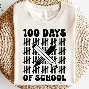 Peut inclure: T-shirt blanc avec du texte noir qui dit "100 jours d'école" avec un graphique de deux crayons croisés l'un sur l'autre. Les crayons sont soulignés en noir et ont une gomme à une extrémité.