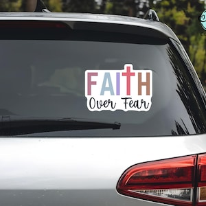 May include: A rectangular sticker on a car window with the words "FAITH Over Fear" in colorful block letters and a cross symbol. The sticker is white with a black outline, and the car is silver.