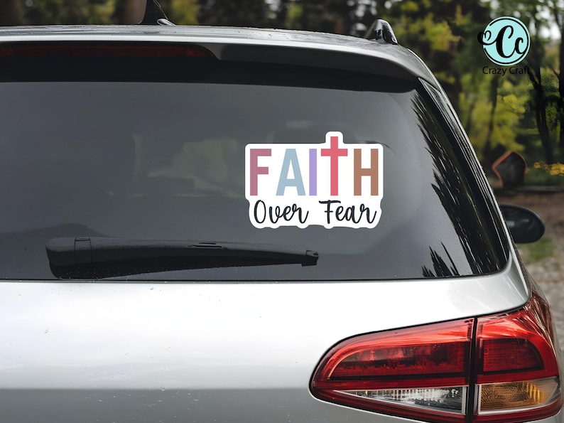 May include: A rectangular sticker on a car window with the words "FAITH Over Fear" in colorful block letters and a cross symbol. The sticker is white with a black outline, and the car is silver.