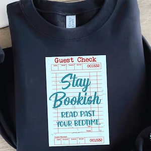 May include: Navy blue sweatshirt with a graphic of a guest check that reads "Stay Bookish, Read Past Your Bedtime." The design is in teal and red on a light blue background. The sweatshirt has a crew neck.